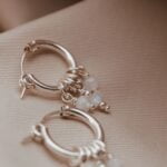 עגילי חישוק בייסיק בשילוב אבני מונסטון אסימטריות לבנות עם השתקפויות של צבעי קשת. העגילים מעוצבים בקווים נקיים, בדוגמא מינימליסטית, קלאסית ועל-זמנית.jpg