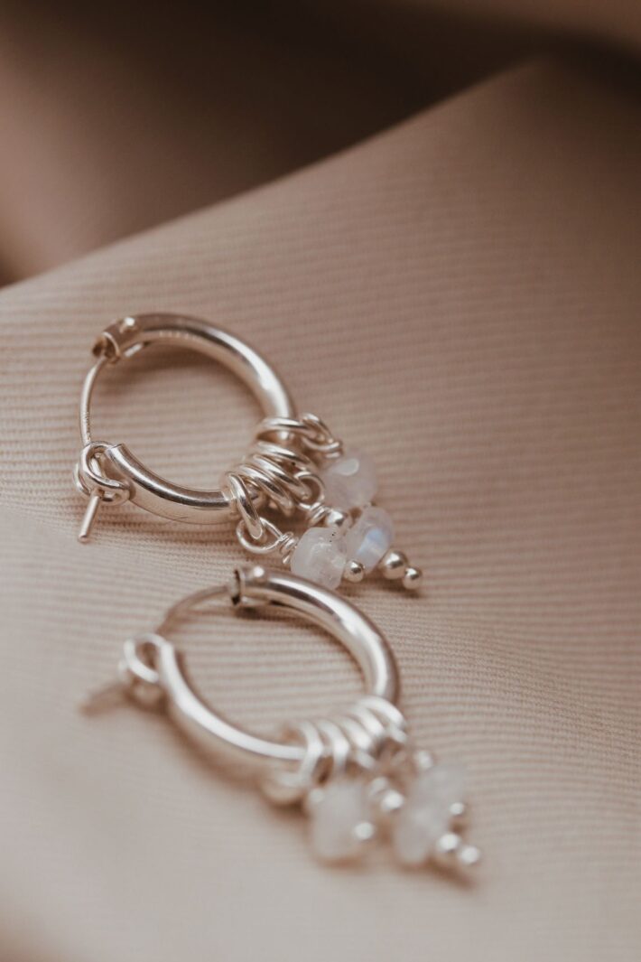 עגילי חישוק בייסיק בשילוב אבני מונסטון אסימטריות לבנות עם השתקפויות של צבעי קשת. העגילים מעוצבים בקווים נקיים, בדוגמא מינימליסטית, קלאסית ועל-זמנית.jpg