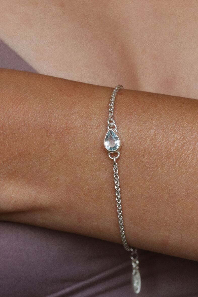 צמיד חבל עדין בשילוב אבן חן טופז טבעית בצורת טיפה ובגווני תכלת פסטלים. מיוצר מכסף 925