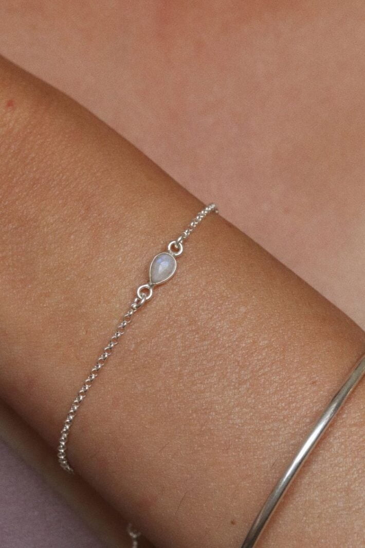 צמיד לולאות עדין בשילוב אבן חן מונסטון קטנה בצורת טיפה ובגווני לבן עם השתקפויות של צבעי קשת. מיוצר מכסף 925 ועמיד במים